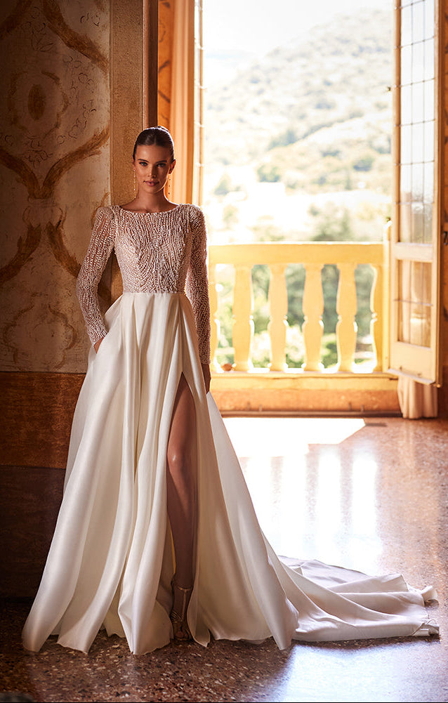 Woman in a white wedding dress standing in a room with a large window.