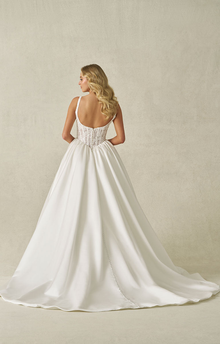 Woman wearing A1406 by Allure Bridal from Abella - Beaded Lace and Satin Ball Gown Wedding Dress with a plain beige wall background