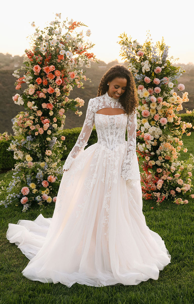 Woman in A1408 by Allure Bridal - Strapless Sequin Lace and Tulle Ball Gown Wedding Dress standing in front of floral decorations.