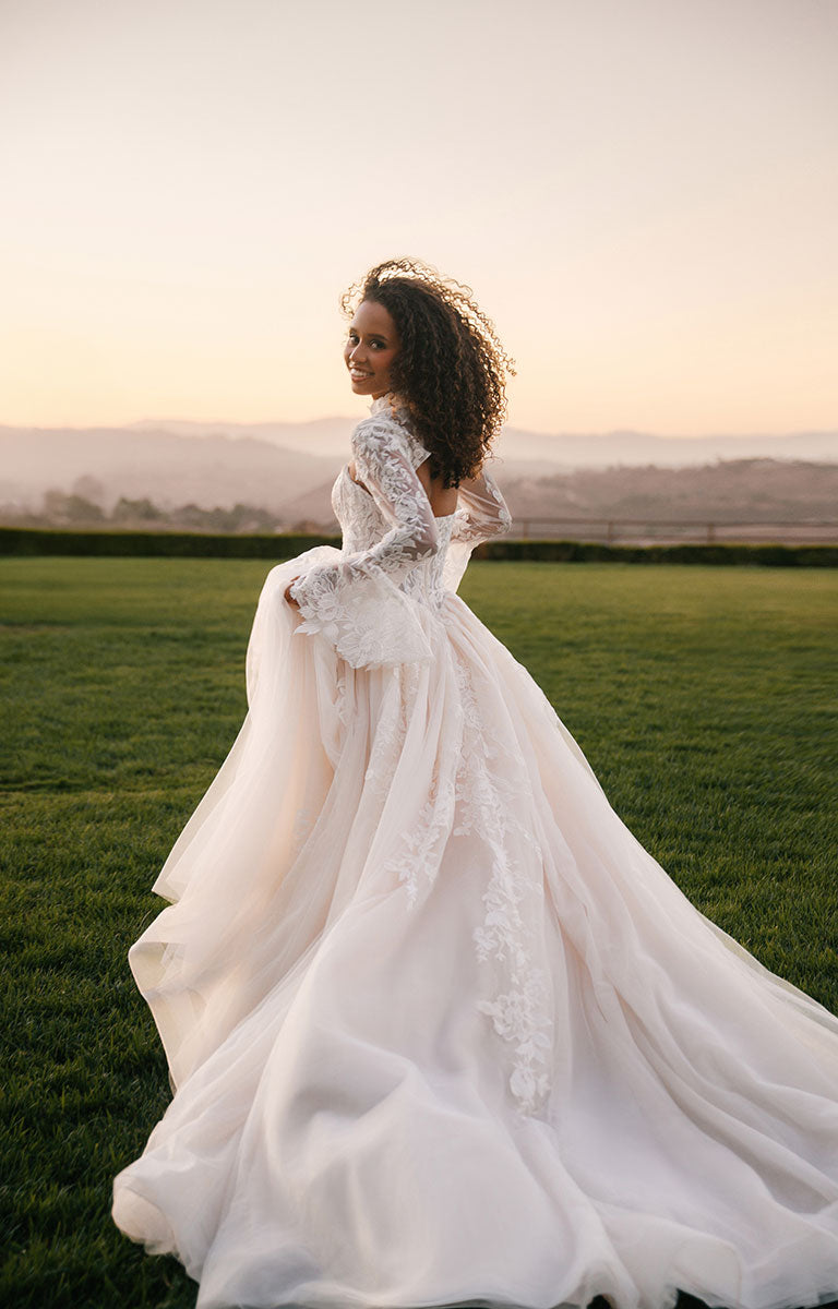 Woman in A1408 by Allure Bridal - Strapless Sequin Lace and Tulle Ball Gown Wedding Dress standing in a field with a sunset in the background