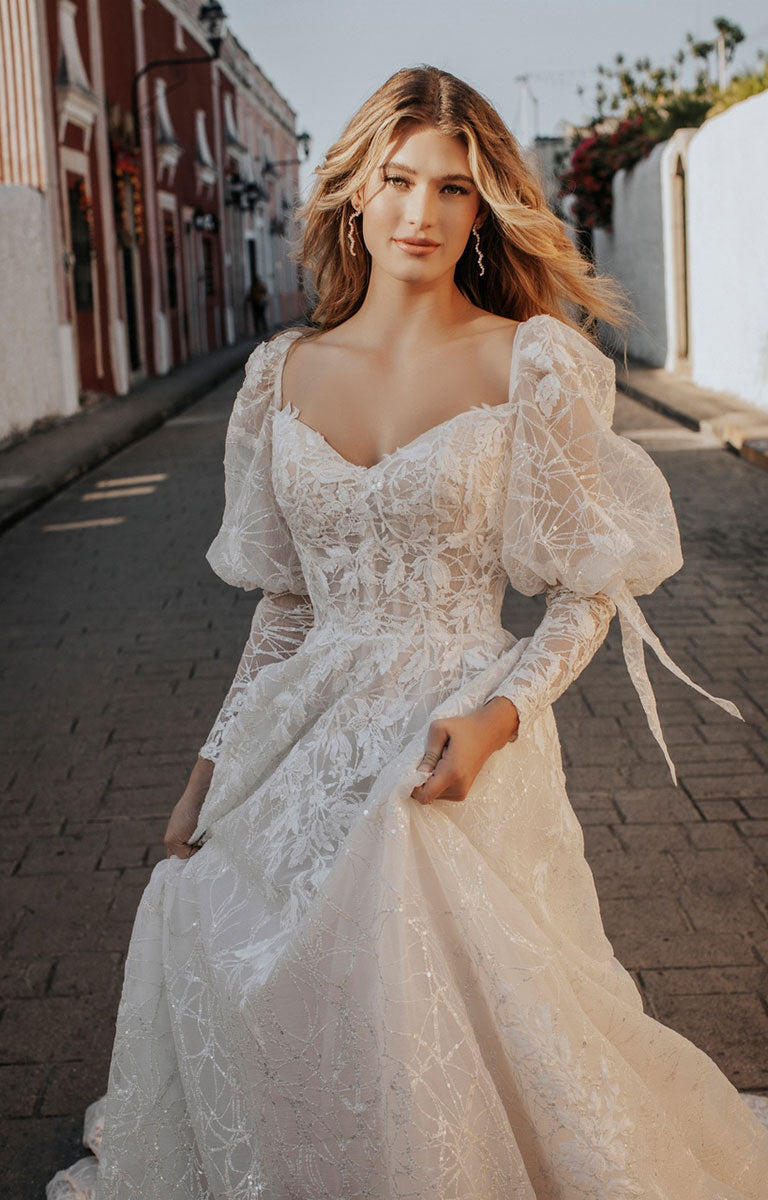 Woman in a lace wedding dress standing on a street.