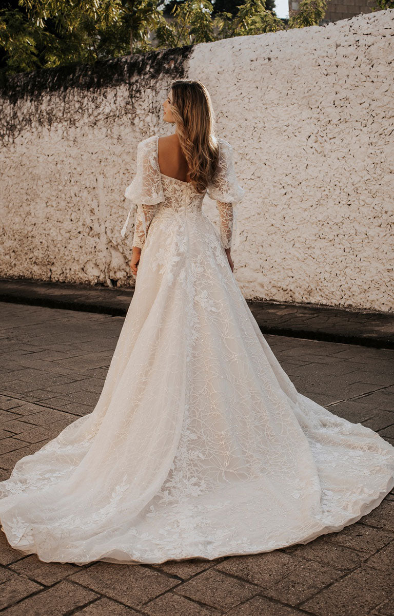 Woman in a white lace wedding dress standing against a textured wall.