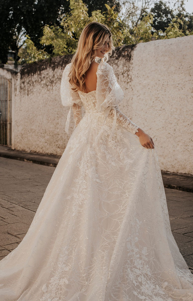 Woman wearing a lace wedding dress with long sleeves in an outdoor setting.