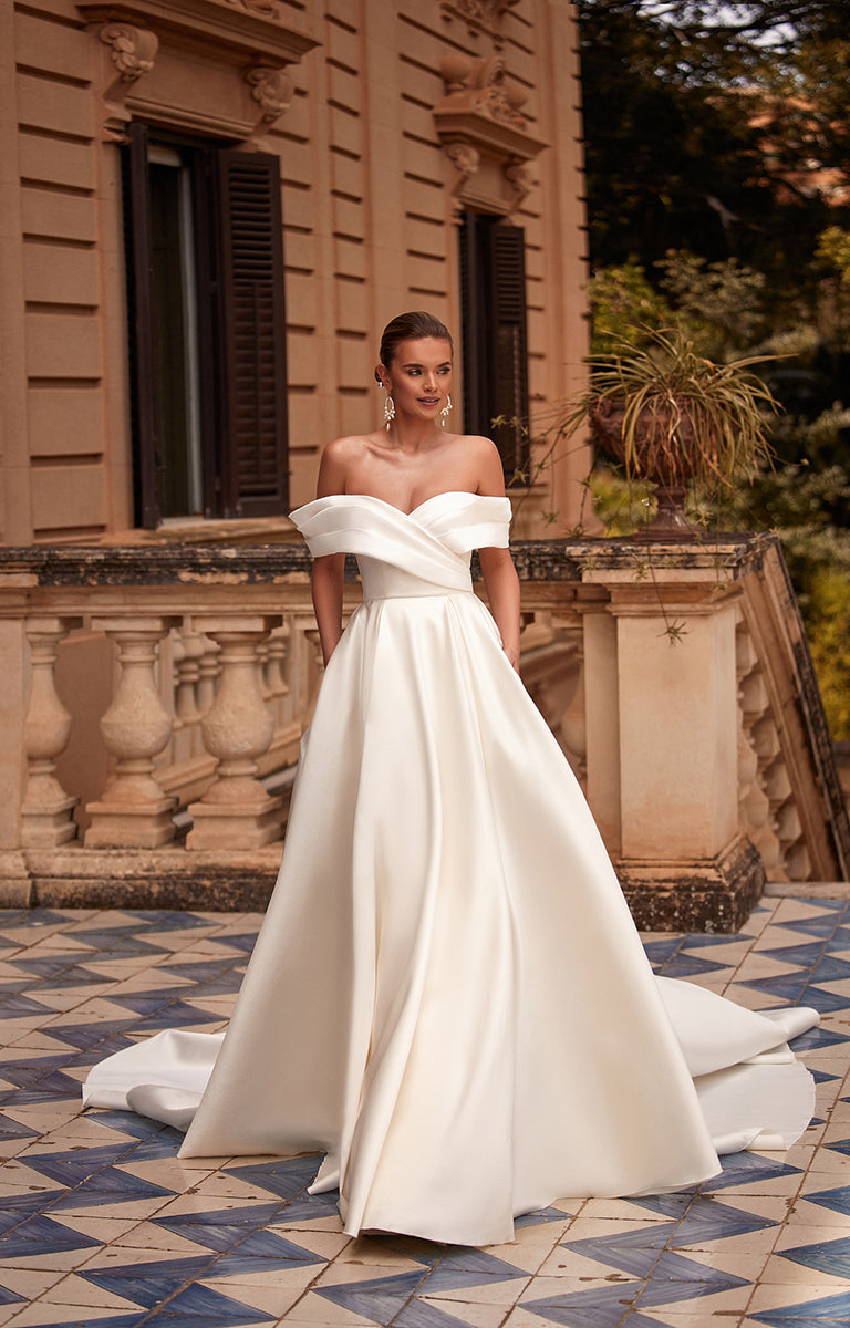 Woman in a white off-shoulder wedding dress standing in front of an elegant building.