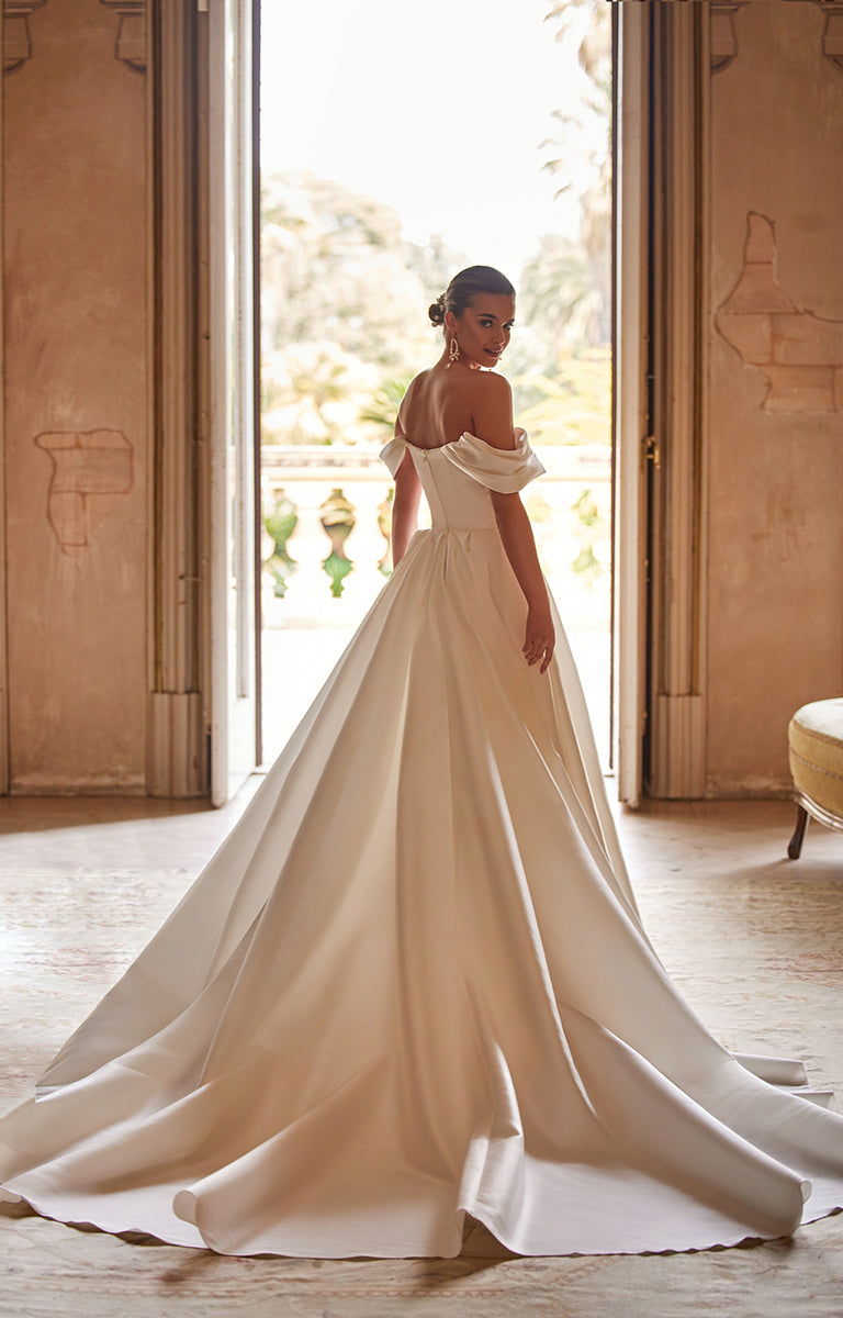 Woman in a white wedding dress standing in a room with large windows.