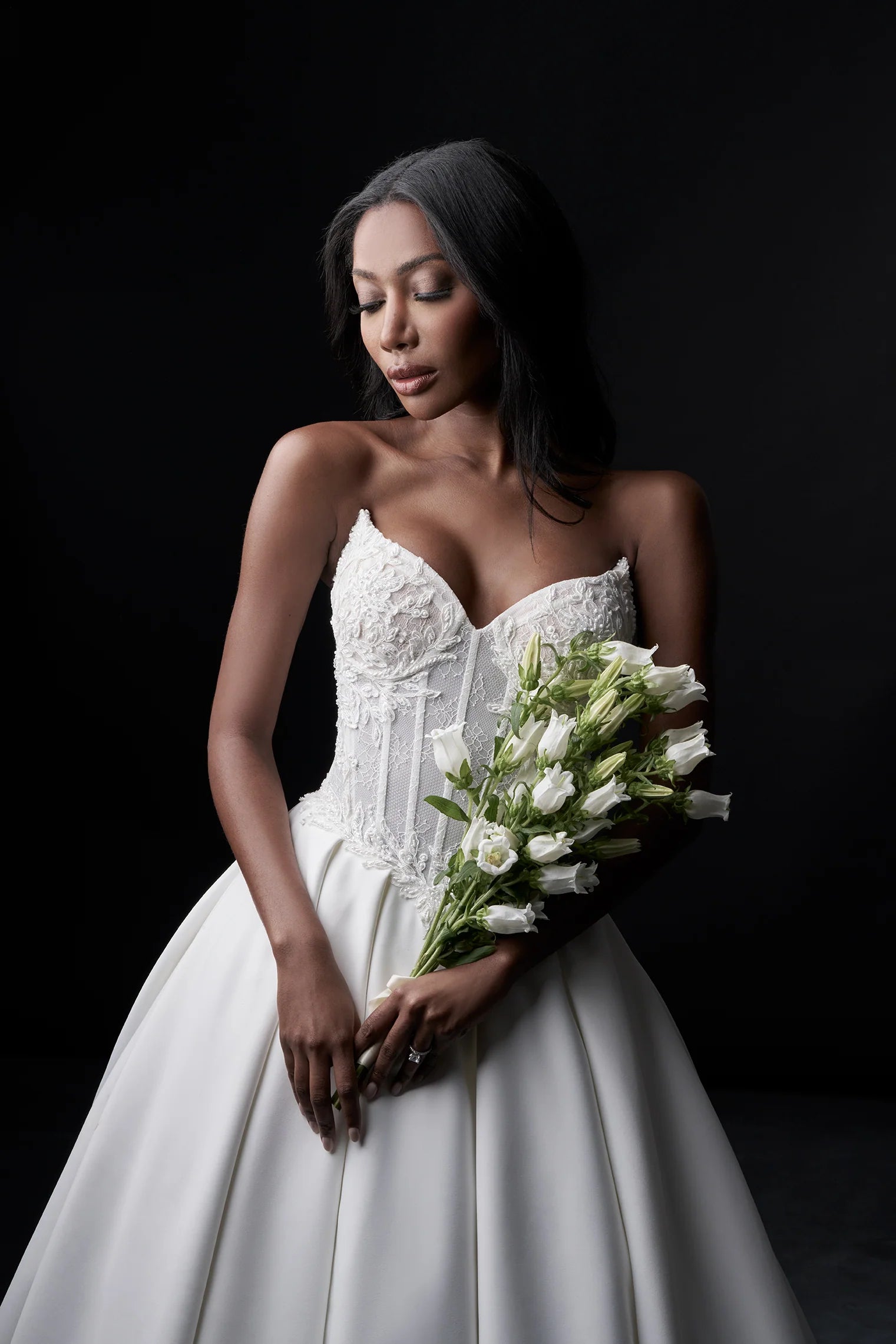Woman in a white wedding dress holding a bouquet against a black background