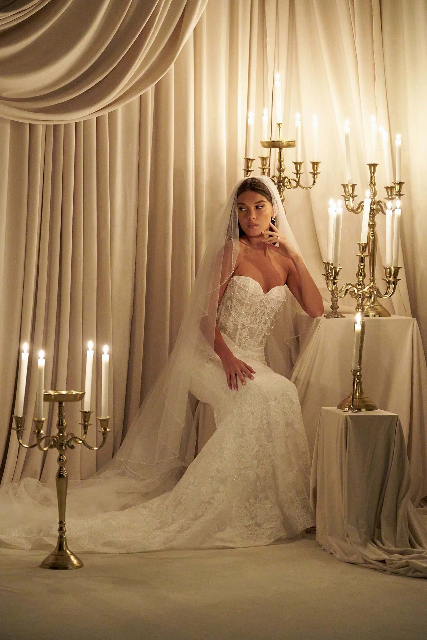 Woman in C803 by Allure Couture - Off-the-Shoulder Embroidered Lace Sheath Wedding Dress with Pearls sitting in a decorated room with candles and candelabras.