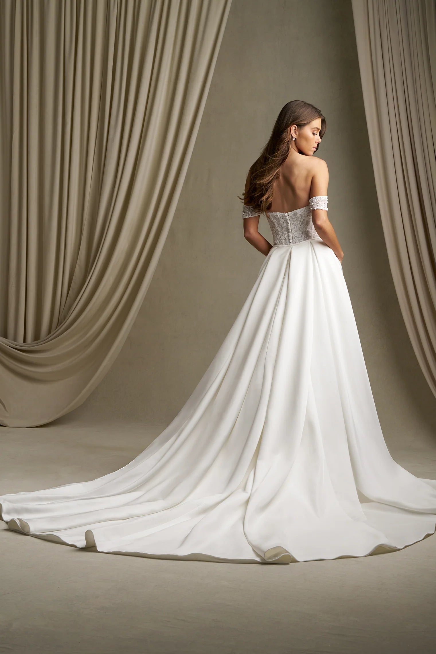 Woman in C803 by Allure Couture - Off-the-Shoulder Embroidered Lace Sheath Wedding Dress with Pearls standing in front of draped curtains.