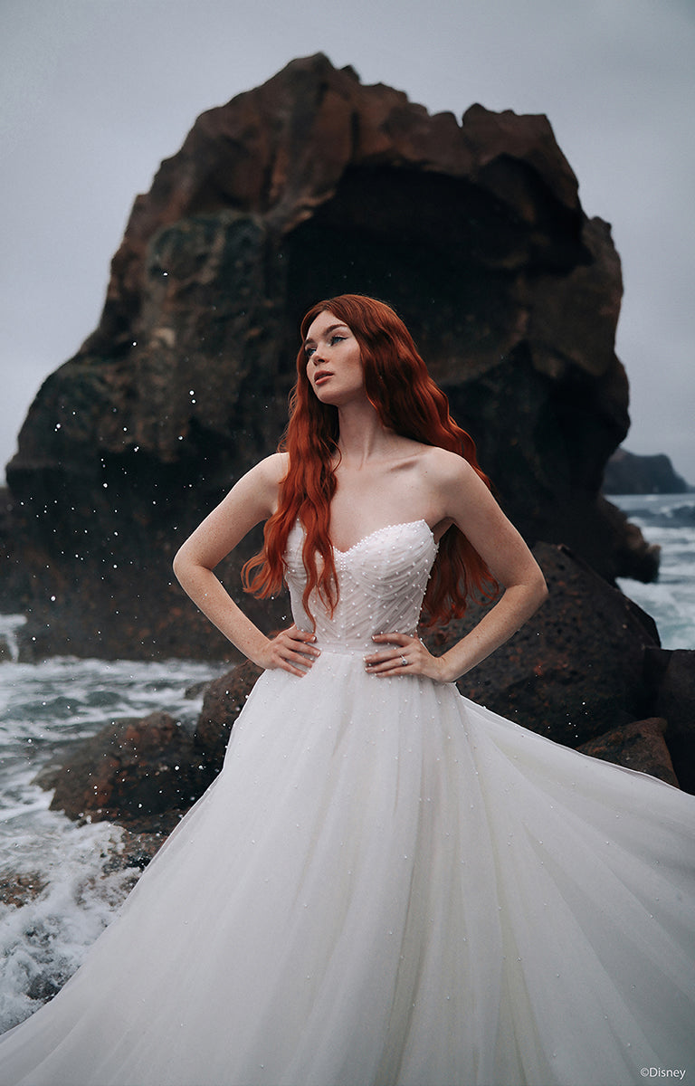 Woman wearing the D440 Ariel - Disney Fairytale Weddings Wedding Dress standing against a rocky coastal background