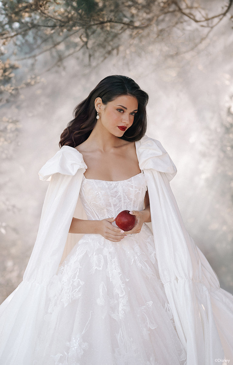 Woman in D447 Snow White - Disney Fairytale Weddings Wedding Dress holding an apple against a snowy background