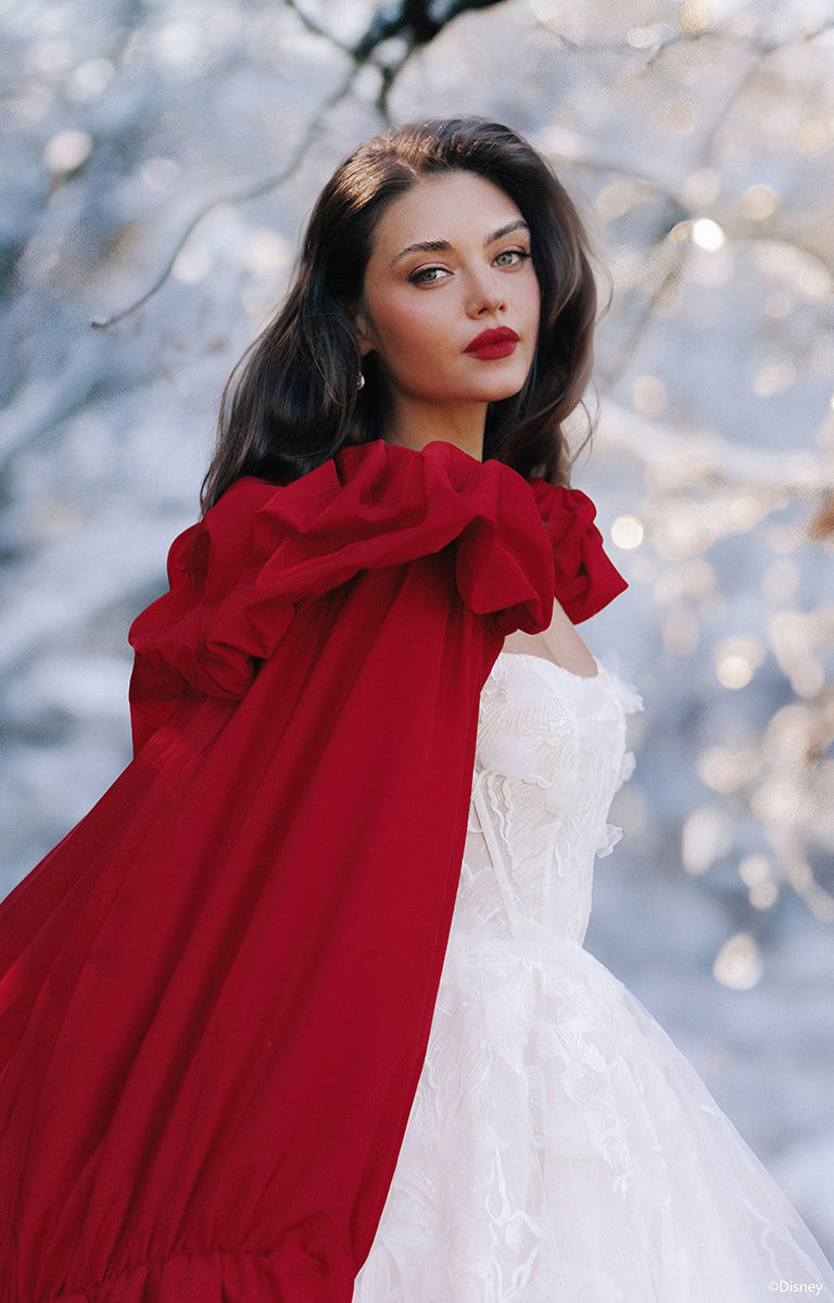 Woman wearing D447 Snow White - Disney Fairytale Weddings Wedding Dress with a red shawl against a snowy background