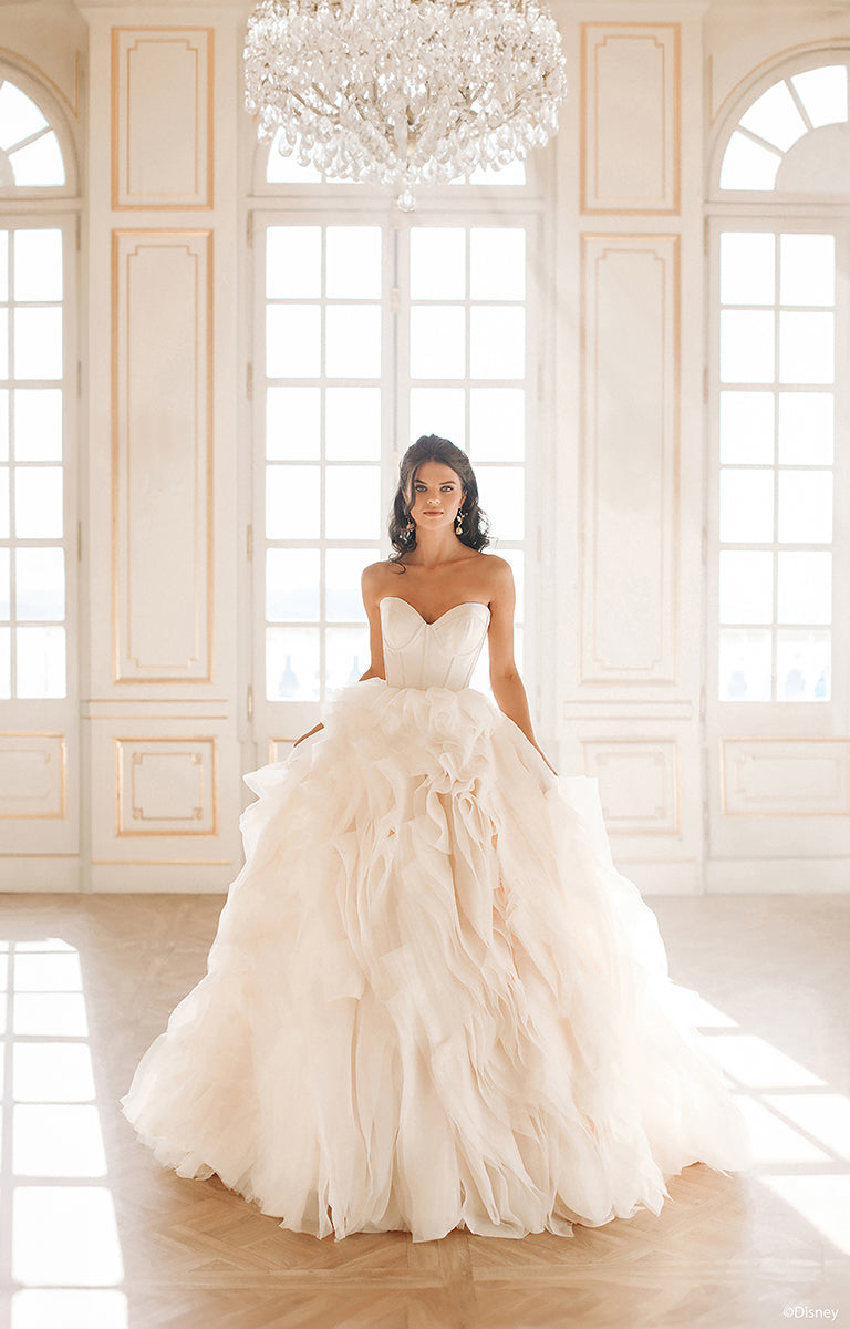 Woman in DP422 Belle - Disney Fairytale Weddings Wedding Dress standing in a grand room with large windows and a chandelier.