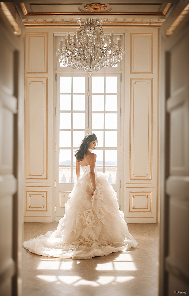 Woman in DP422 Belle - Disney Fairytale Weddings Wedding Dress standing in a grand room with a chandelier.