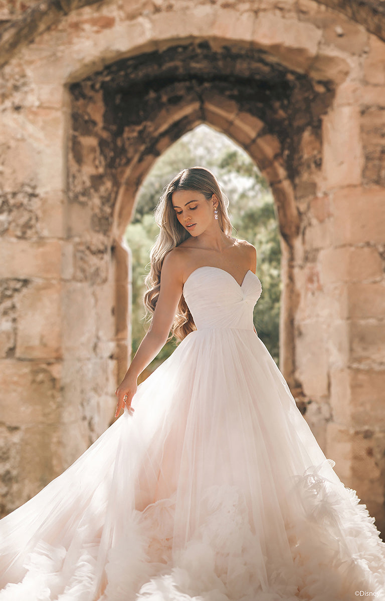 Woman in DP426 Rapunzel - Disney Fairytale Weddings Wedding Dress standing in front of stone arches.