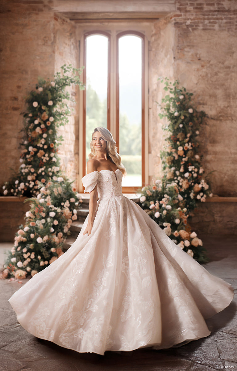 Woman in DP451 Sleeping Beauty - Disney Fairytale Weddings Wedding Dress standing in a room with floral decorations and large windows.