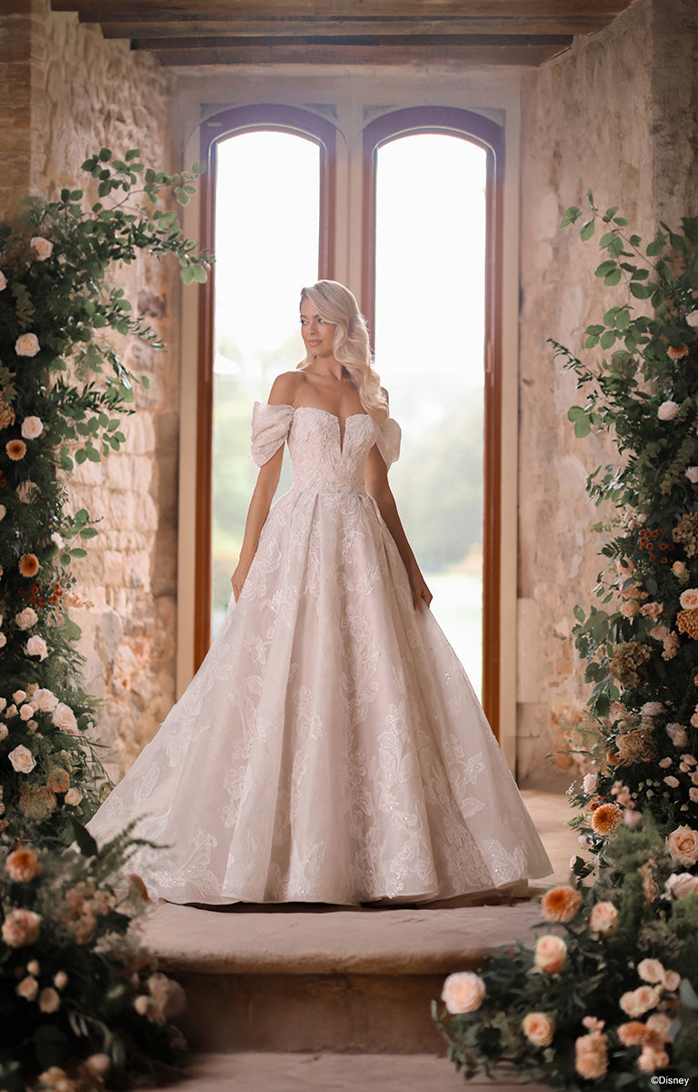 Woman in DP451 Sleeping Beauty - Disney Fairytale Weddings Wedding Dress standing in front of a large window with floral decorations.