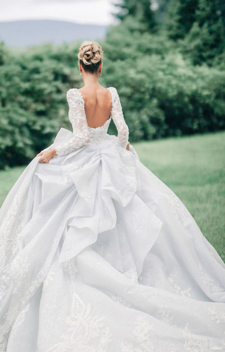 Lady showcasing the rear of the DP453 Cinderella Wedding Dress she is wearing from the Disney Fairytale Weddings collection in front of the gardens of a Castle's countryside setting.