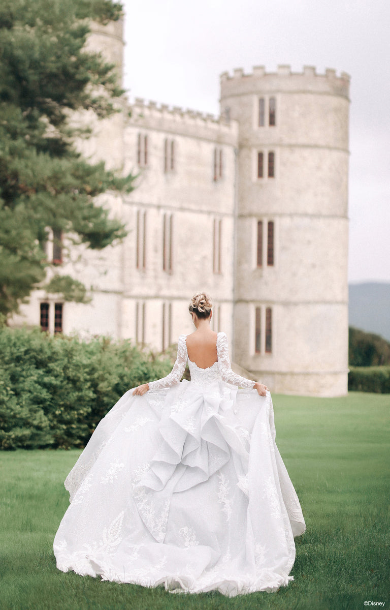 Lady showcasing the rear of the DP453 Cinderella Wedding Dress she is wearing from the Disney Fairytale Weddings collection in front a beautiful Castle..