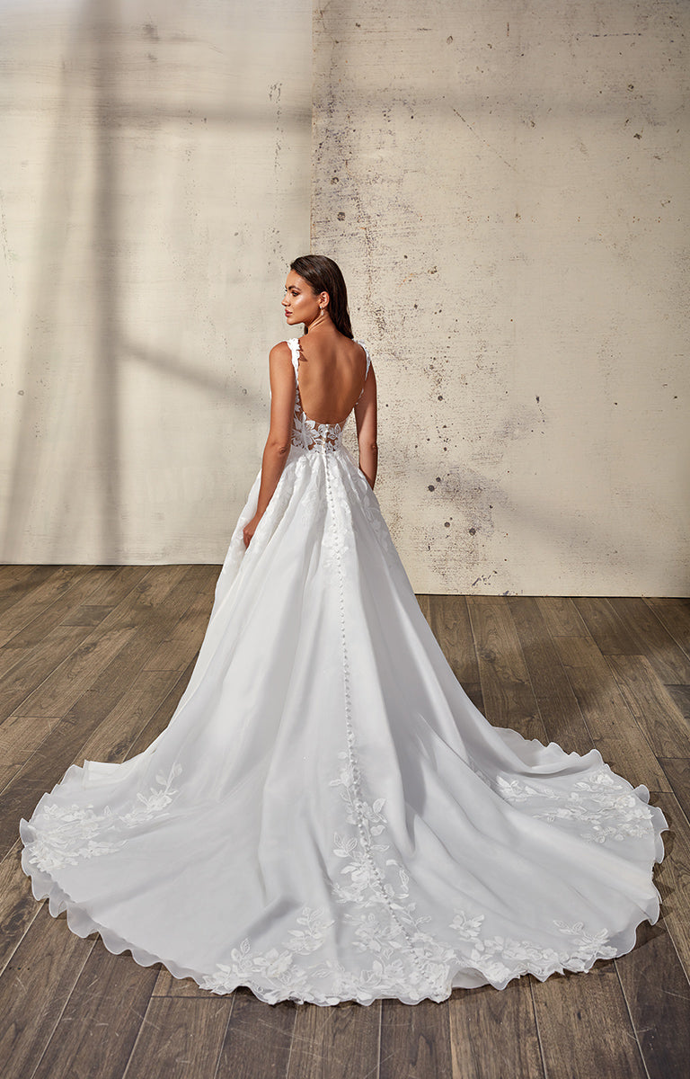 Woman in a white wedding dress with a long train standing in a room with wooden floor and concrete wall.