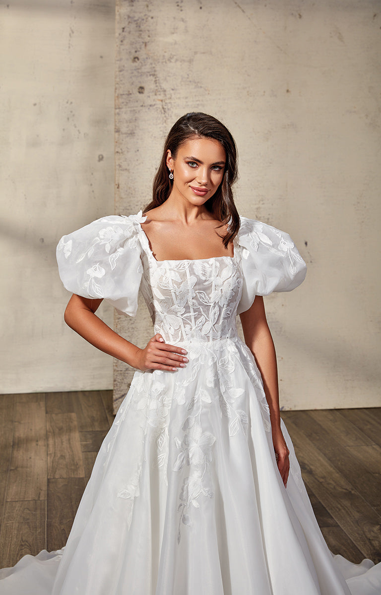 Woman wearing a white wedding dress with puffed sleeves against a neutral background