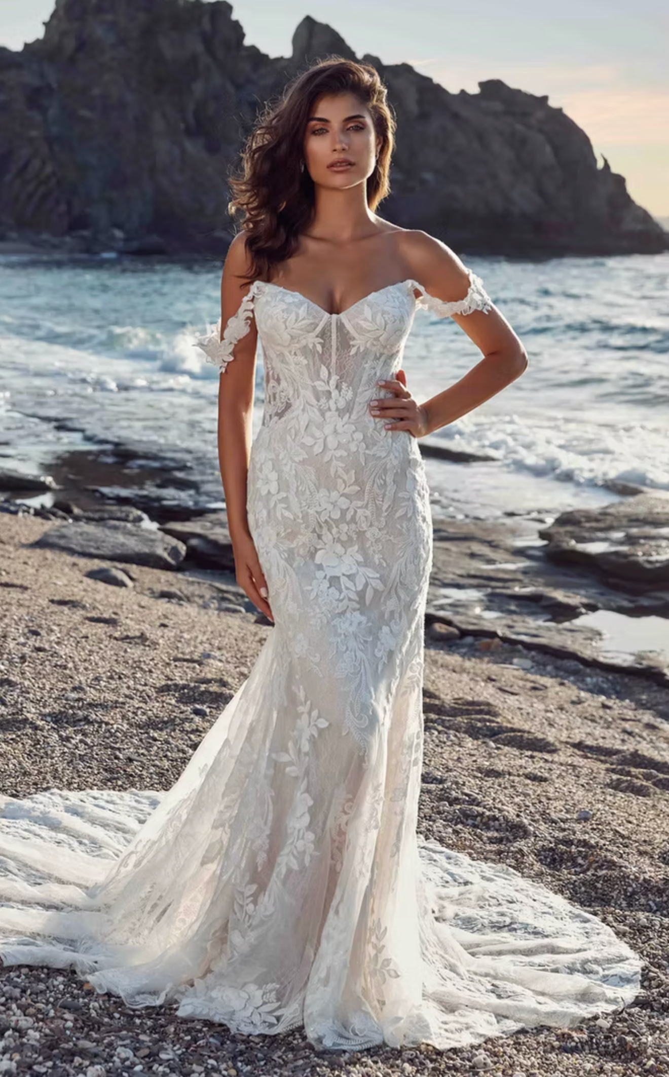 Woman in a white wedding dress standing on a rocky beach.