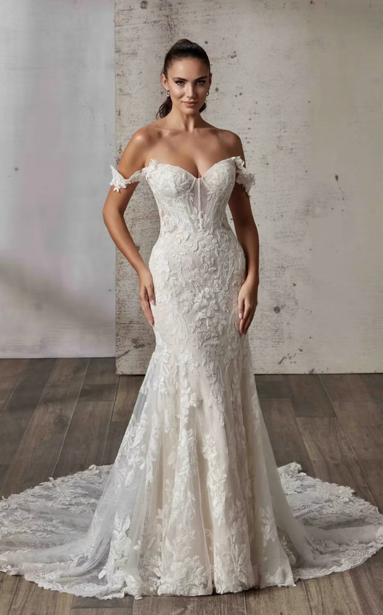 Woman wearing a white lace wedding dress with a long train against a textured wall.