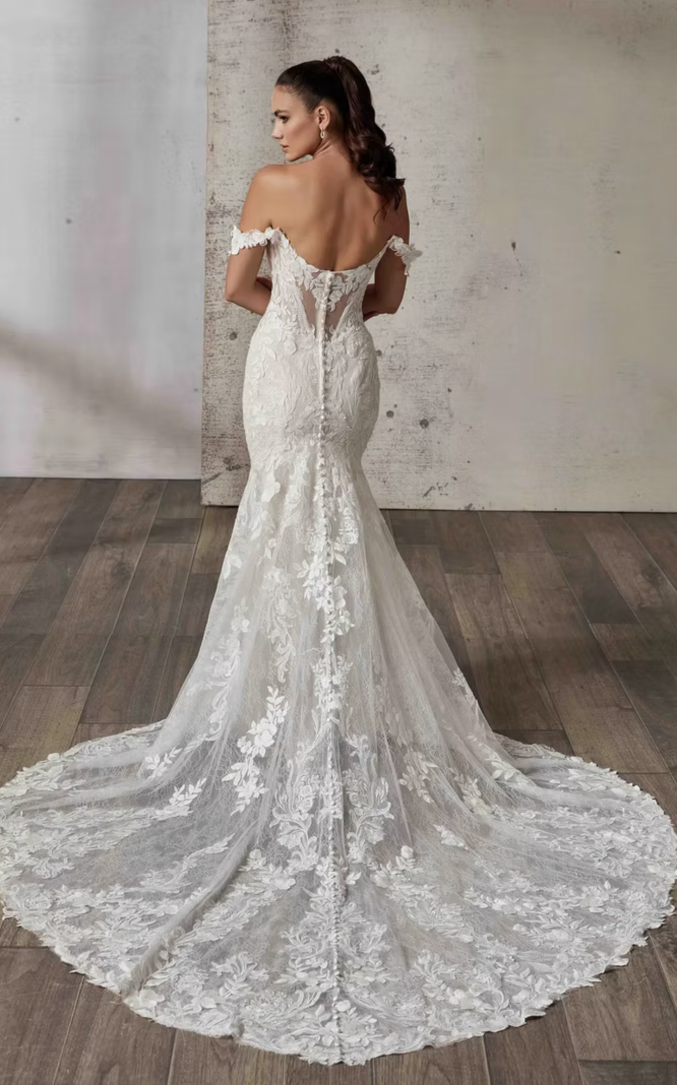 Woman wearing a lace wedding dress with a long train in a minimalistic setting.