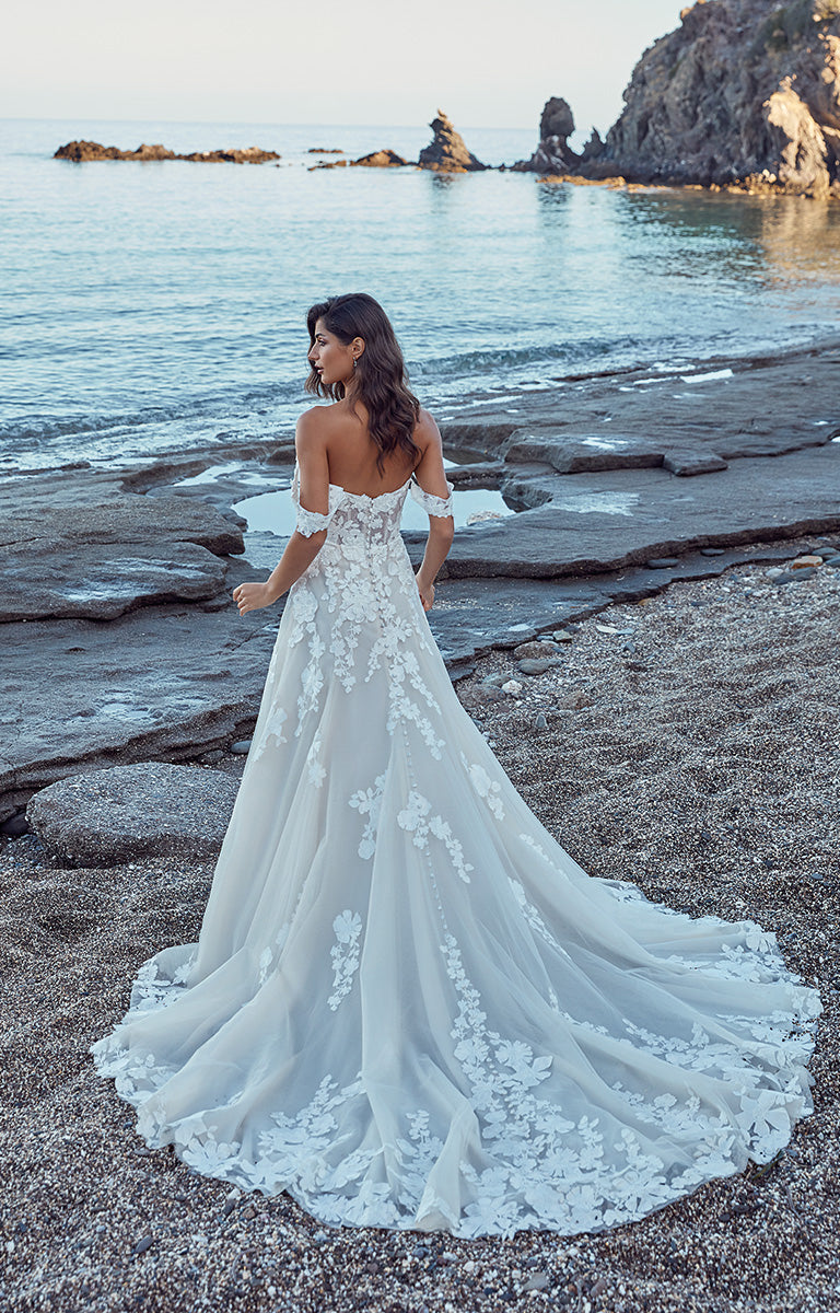 Woman in a white wedding dress standing on a rocky beach with ocean and cliffs in the background