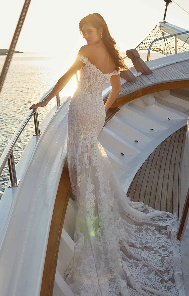 A woman wearing Rio DR2706 by Eddy K Dreams - Ivory and Lavender Lace Fit-and-Flare Wedding Dress stands on the deck of a boat at sunset, with the ship's white railing and wooden steps visible around her.