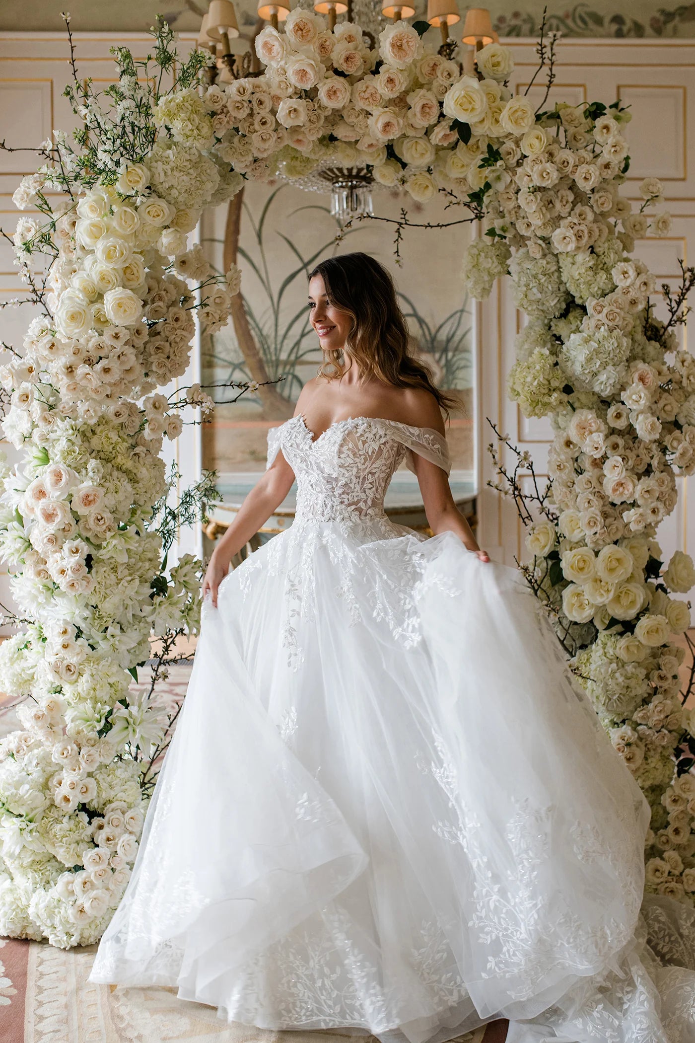 Woman in a white wedding dress standing in front of a floral archway.