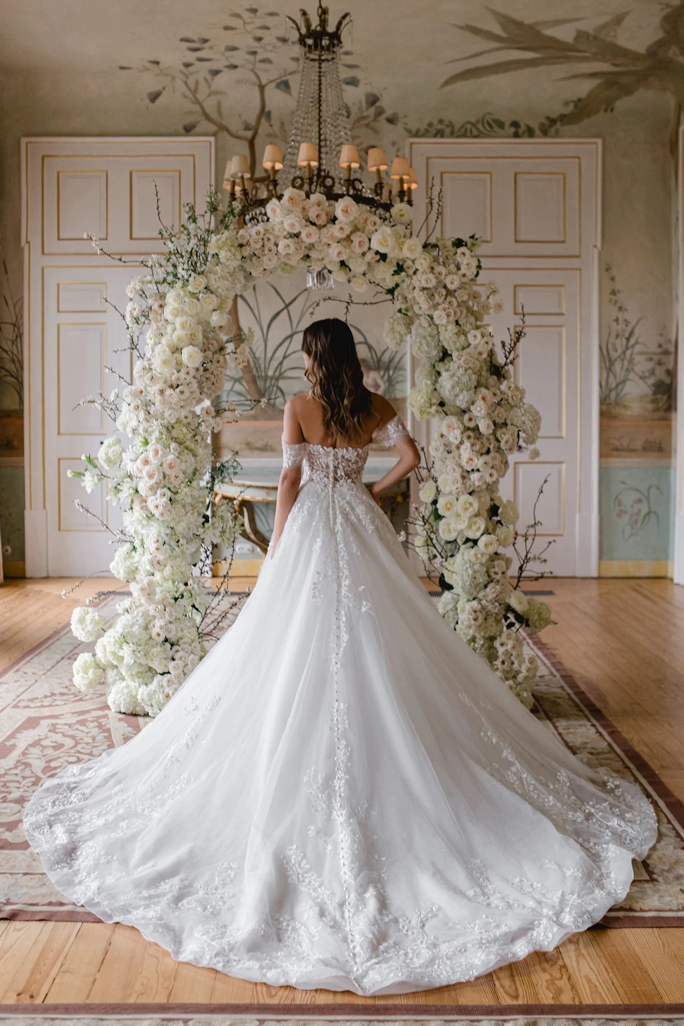 Woman in a white wedding dress standing in front of a floral archway.