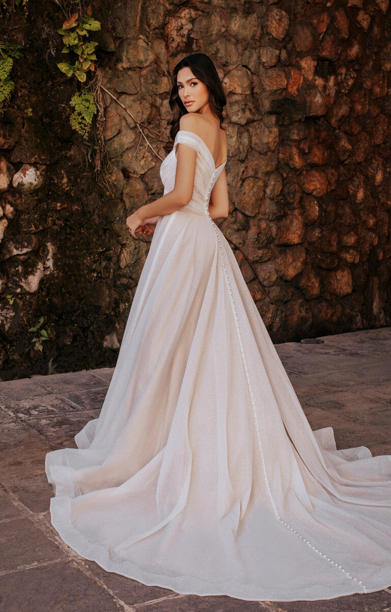 Woman in a white wedding dress standing against a stone wall.