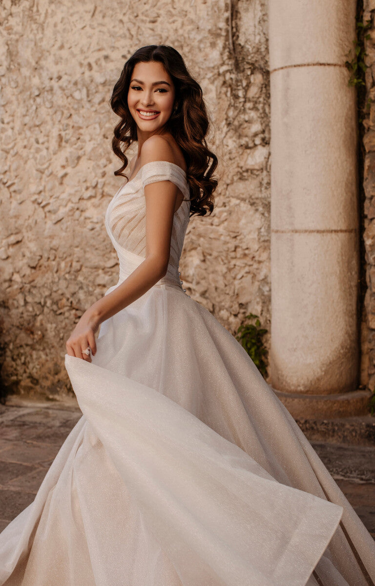 Woman in a white wedding dress standing against a stone wall.