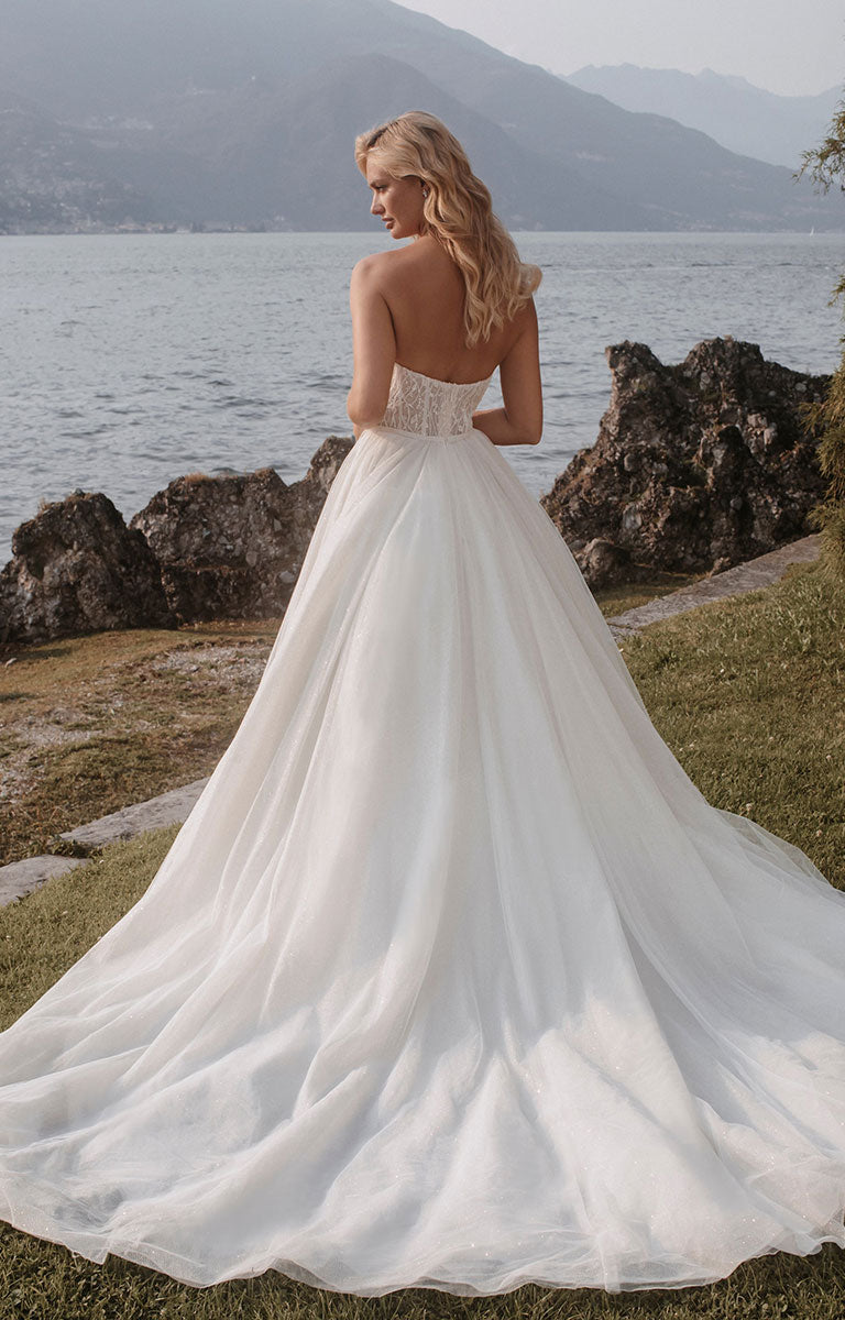Woman wearing Stella E405 by Abella - Strapless Sparkle Tulle Ballgown Wedding Dress with a lake and mountain backdrop.