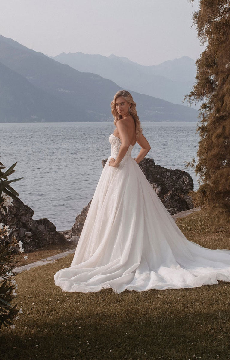 Woman wearing Stella E405 by Abella - Strapless Sparkle Tulle Ballgown Wedding Dress with a lake and mountain backdrop.