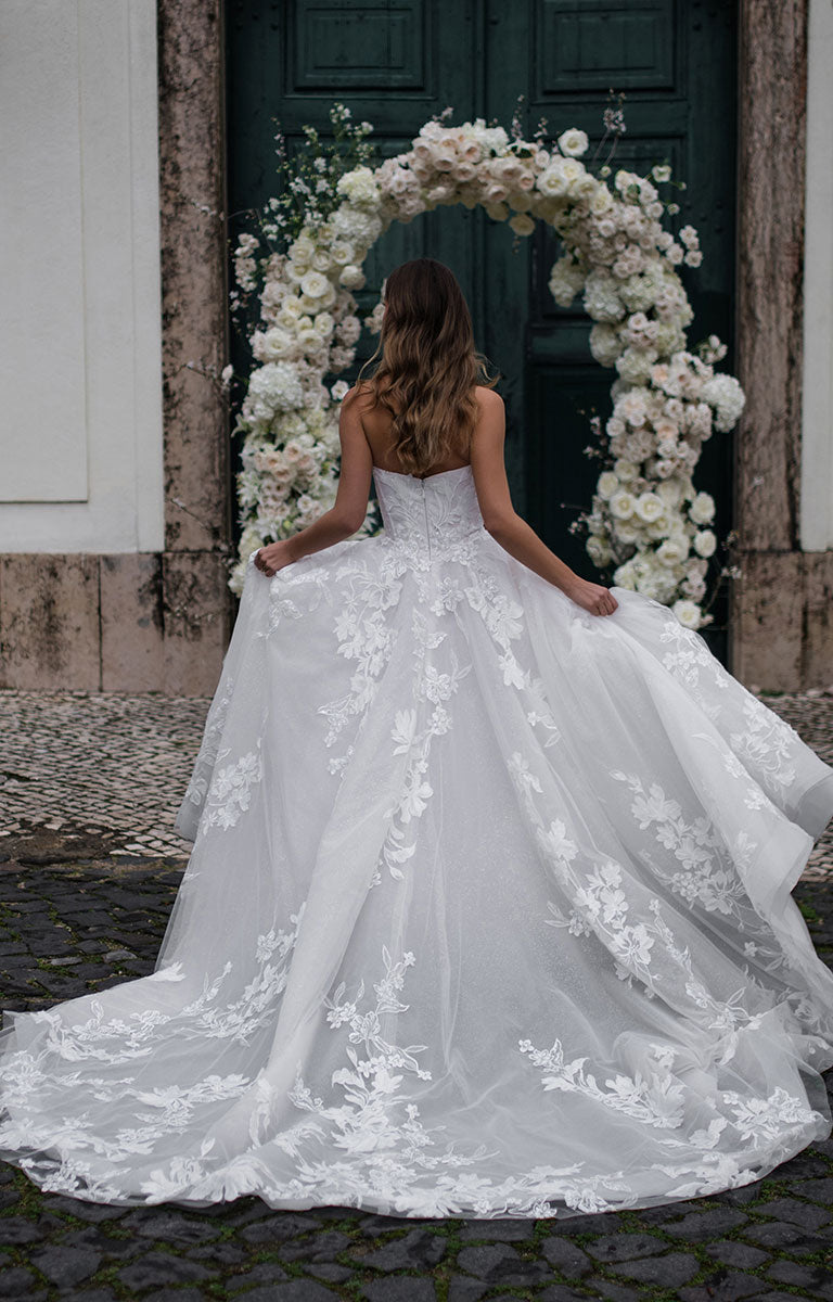 Woman in a white wedding dress standing in front of a floral archway.