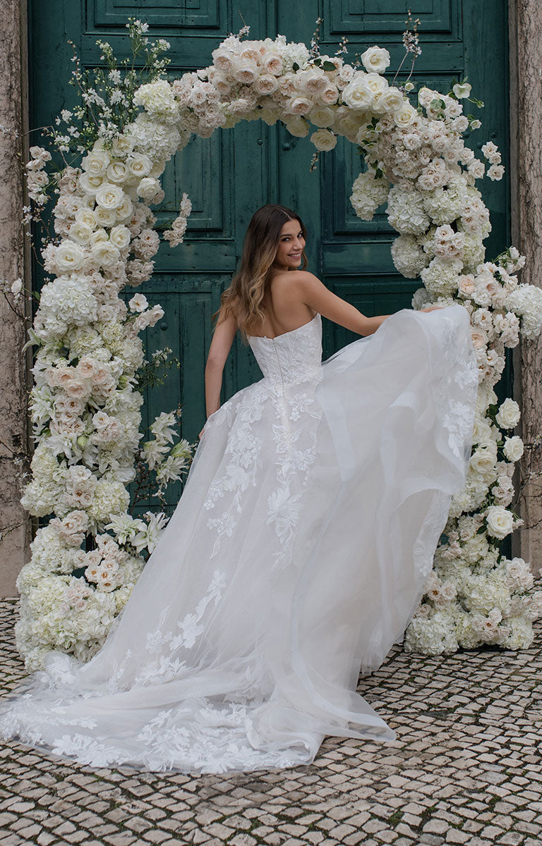 Woman in a white wedding dress standing in front of a floral archway.