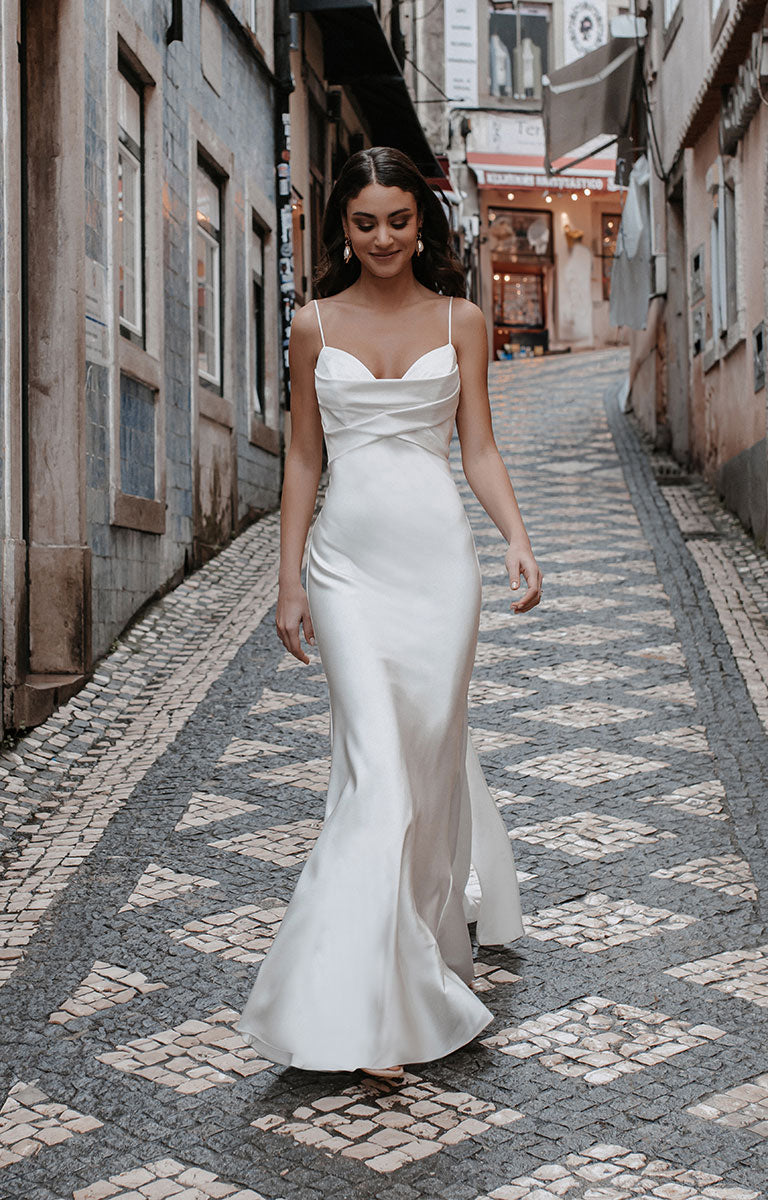 Woman in a white dress walking down a narrow street with buildings on either side.
