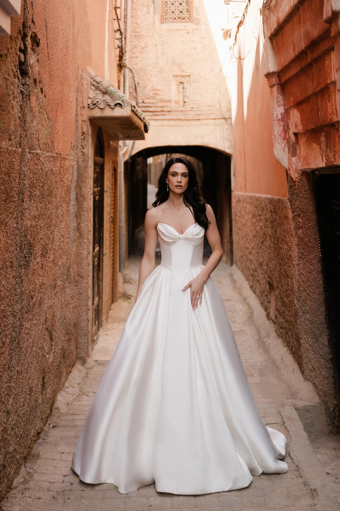 Woman in a white wedding dress standing in a narrow alleyway with warm-toned walls.