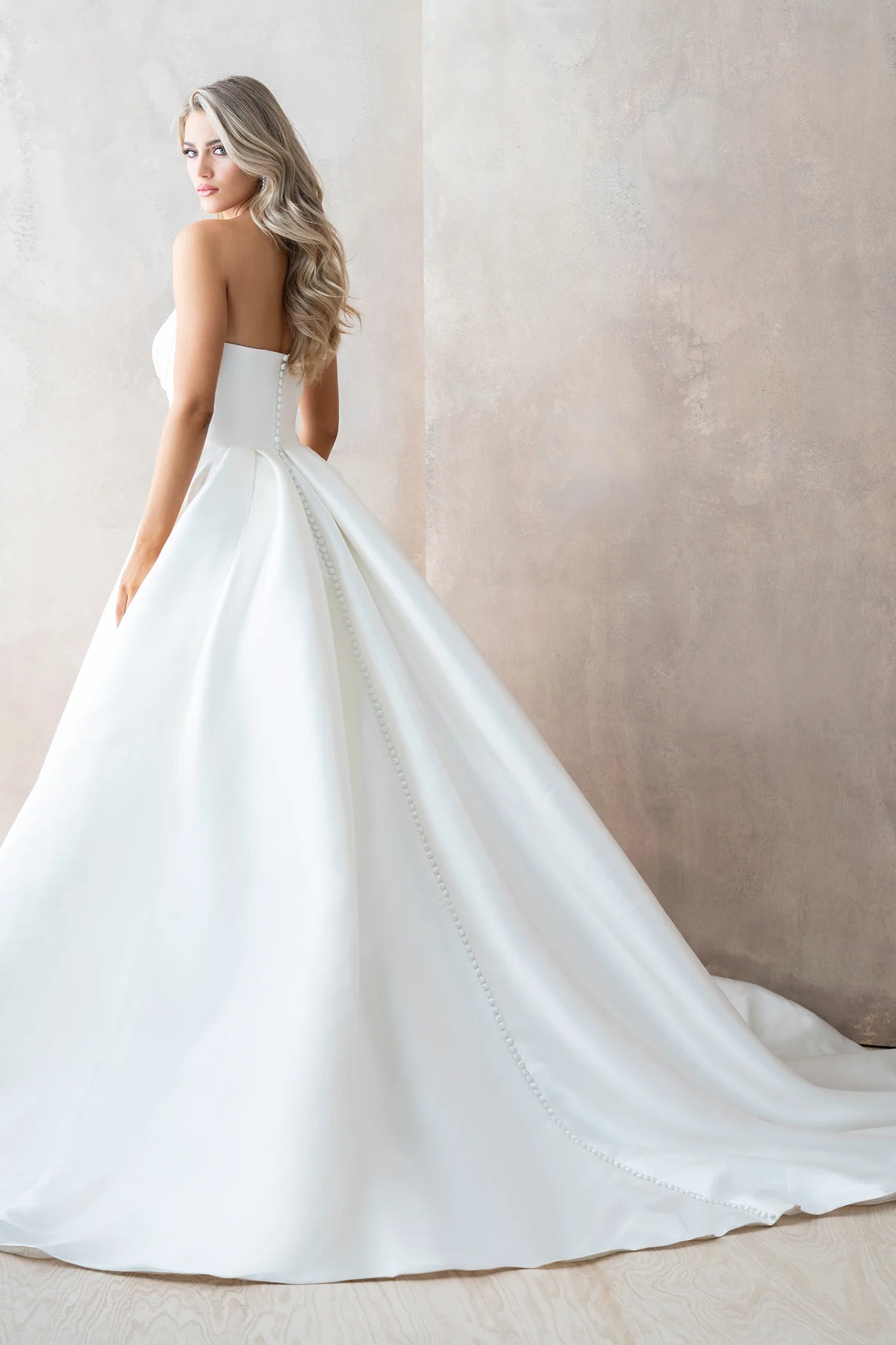 Woman wearing a white strapless wedding dress against a plain background