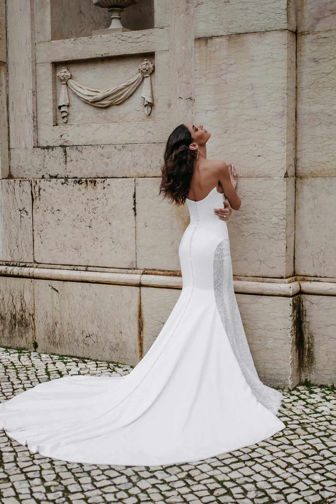 Woman in a white wedding dress standing against a stone wall.