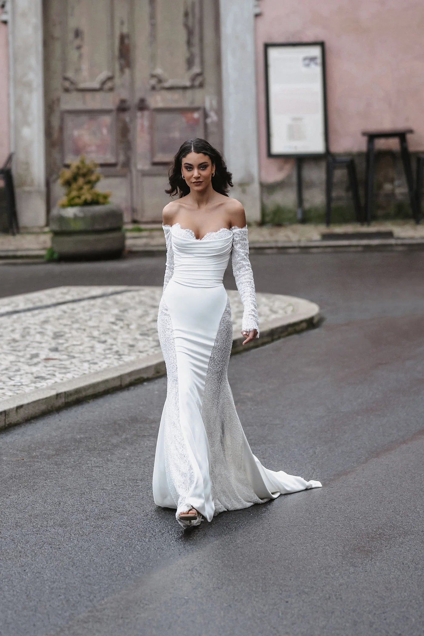 Woman in a white off-shoulder gown walking on a street.