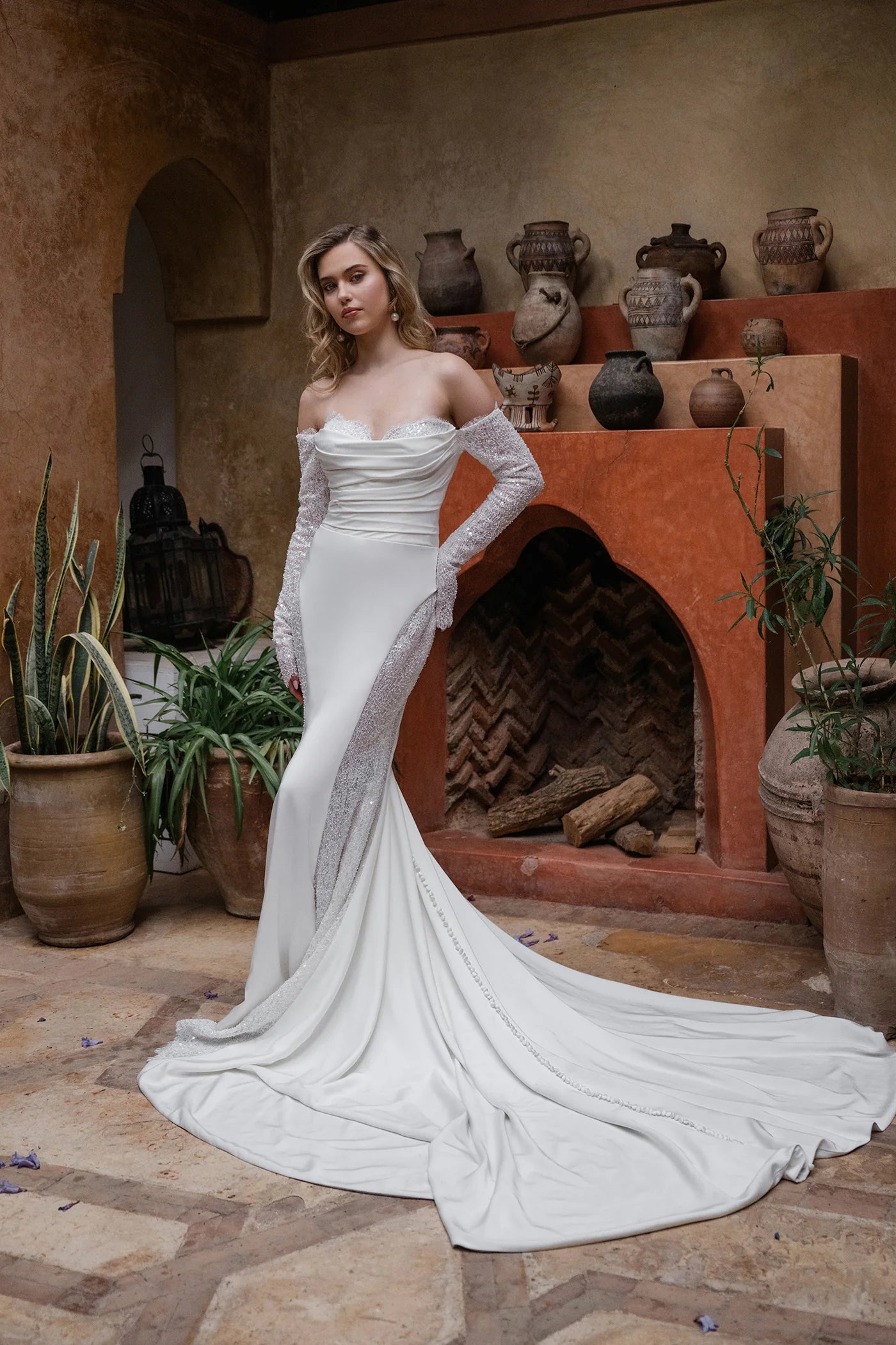 Woman in a white wedding dress standing in a rustic outdoor setting with potted plants and clay pots.