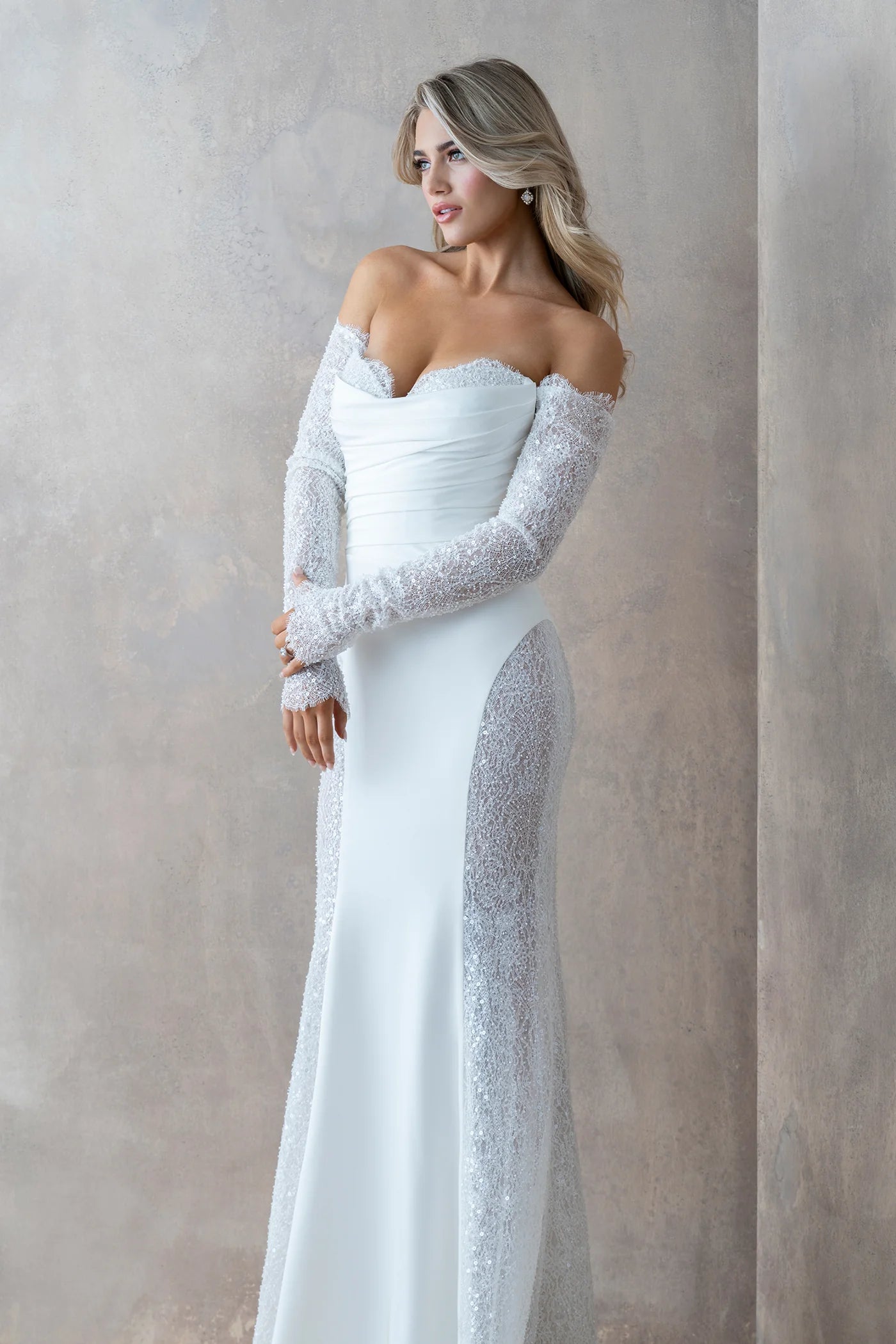 Woman wearing a white off-shoulder gown with lace sleeves against a neutral background
