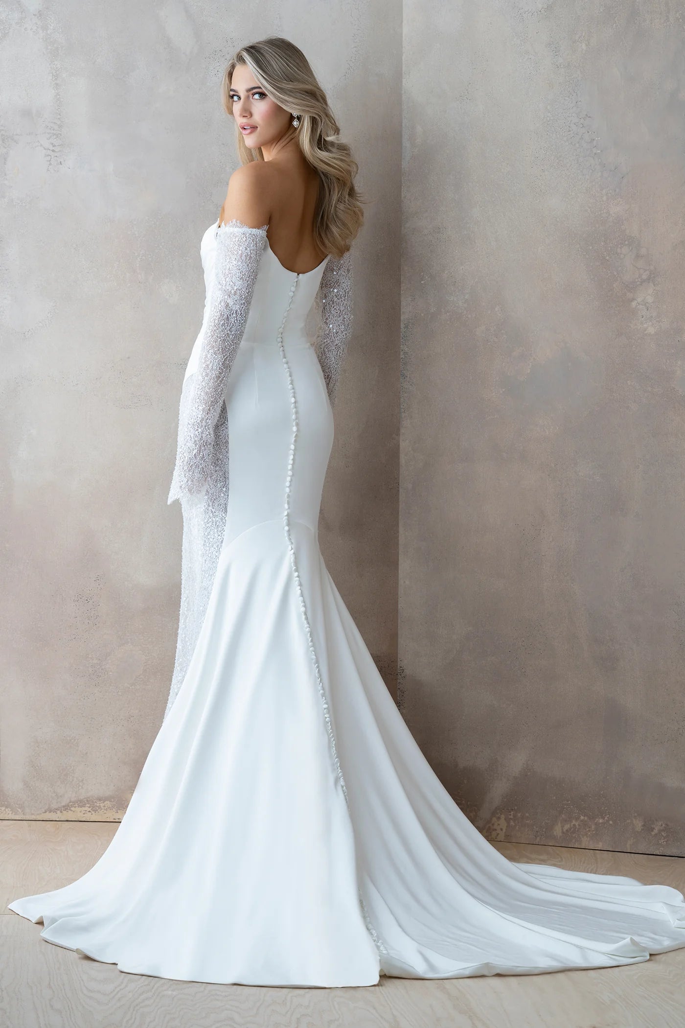 Woman wearing a white wedding dress with a long train against a neutral background