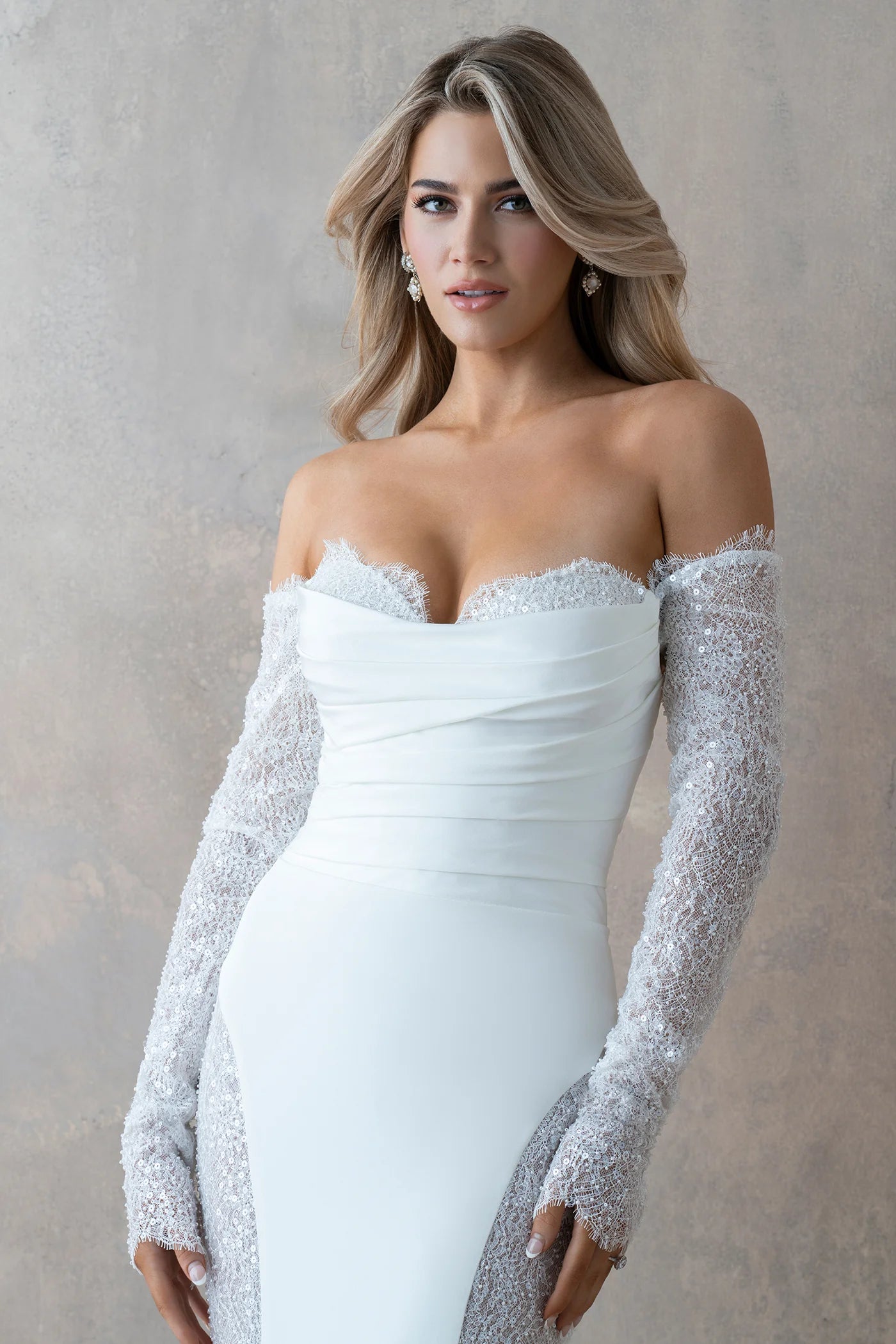 Woman wearing a white off-shoulder dress with silver long sleeves against a neutral background