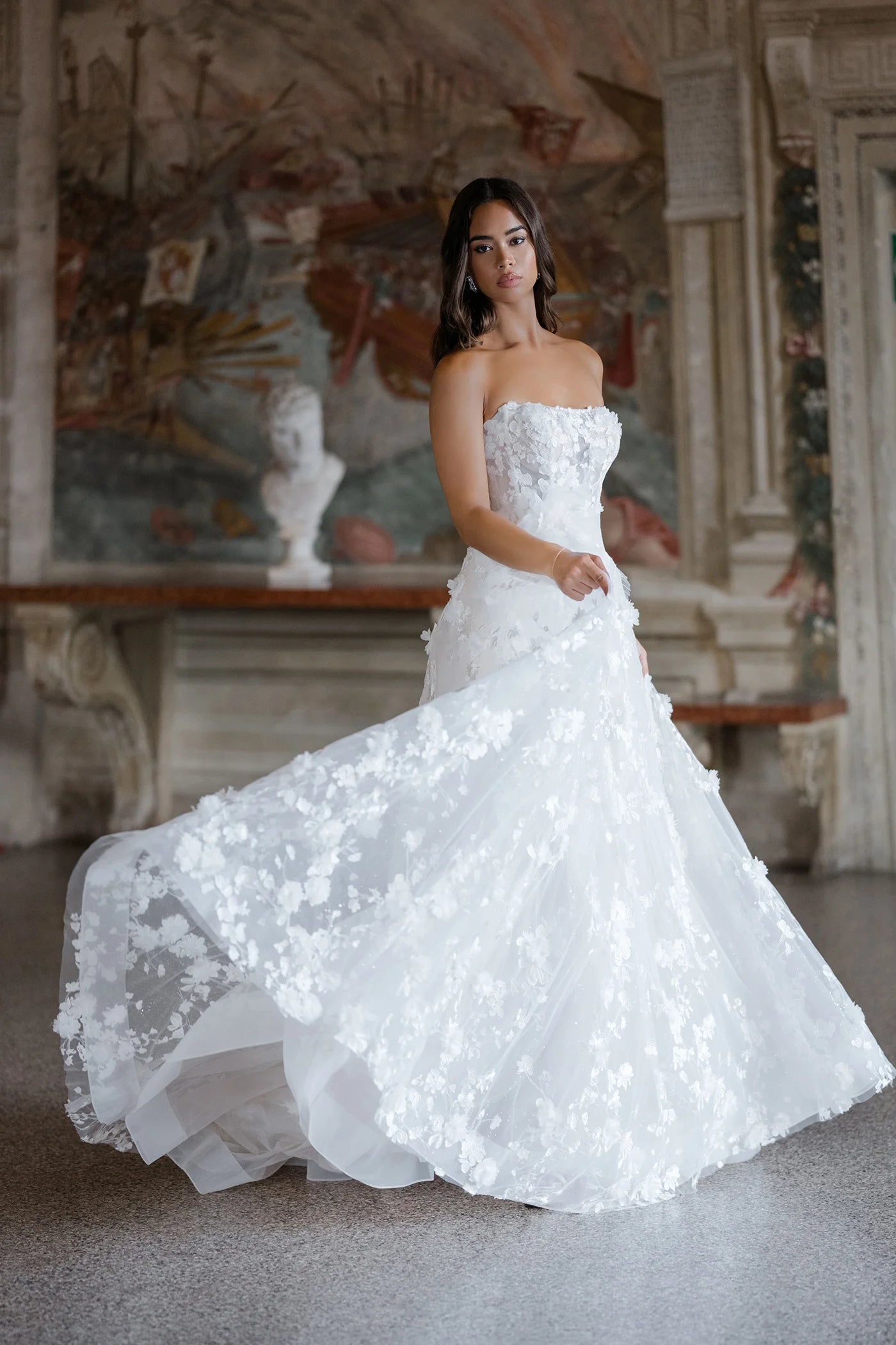 Woman in a white wedding dress standing in an elegant indoor setting.