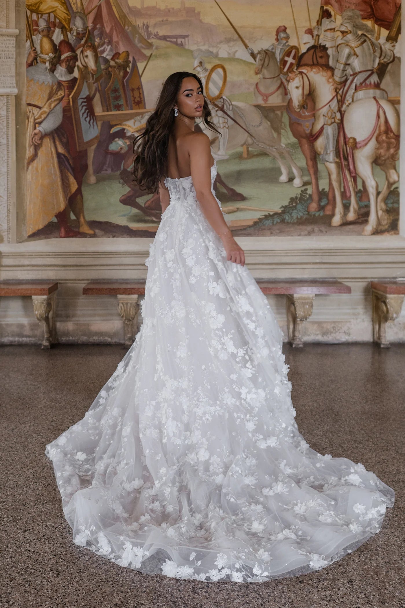 Woman in a white floral wedding dress standing in front of a mural.