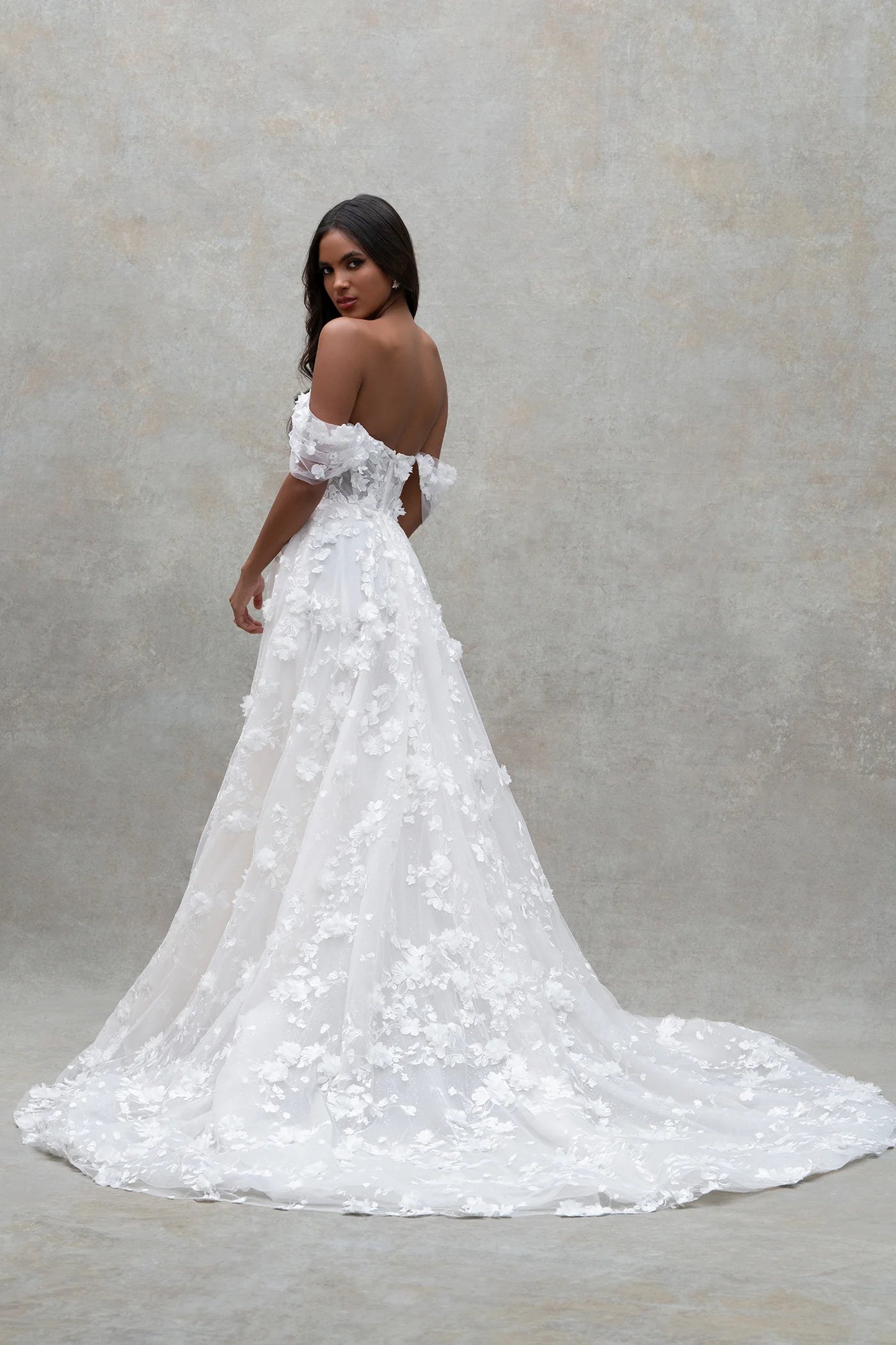 Woman wearing a white wedding dress with floral details against a neutral background