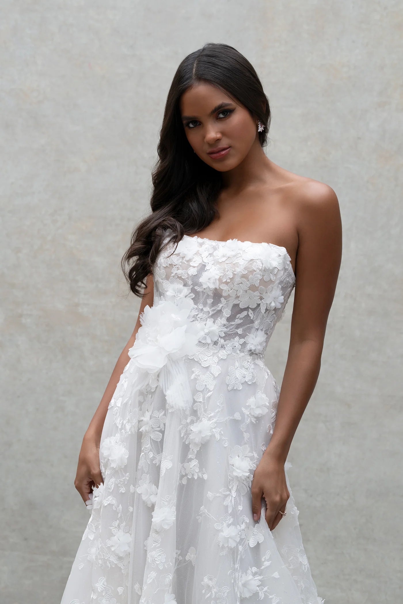 Woman wearing a strapless white lace wedding dress against a plain background